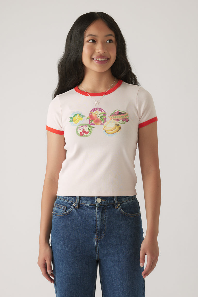 Girl wearing a fitted white cropped tee with red trim and colorful fruit graphics, paired with dark blue denim jeans