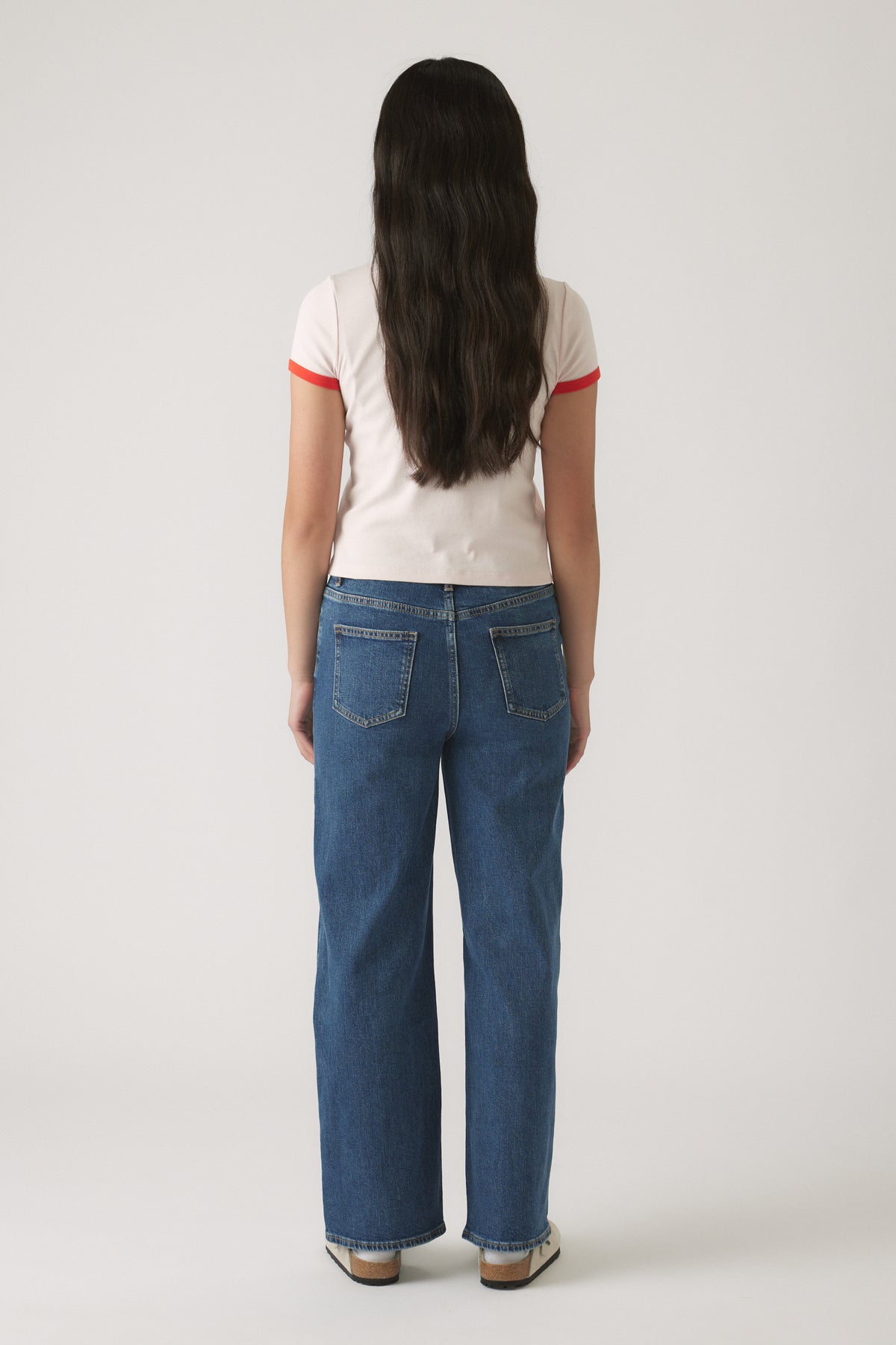 Girl shown from behind wearing a cropped white tee with red trim paired with relaxed straight-leg blue denim jeans