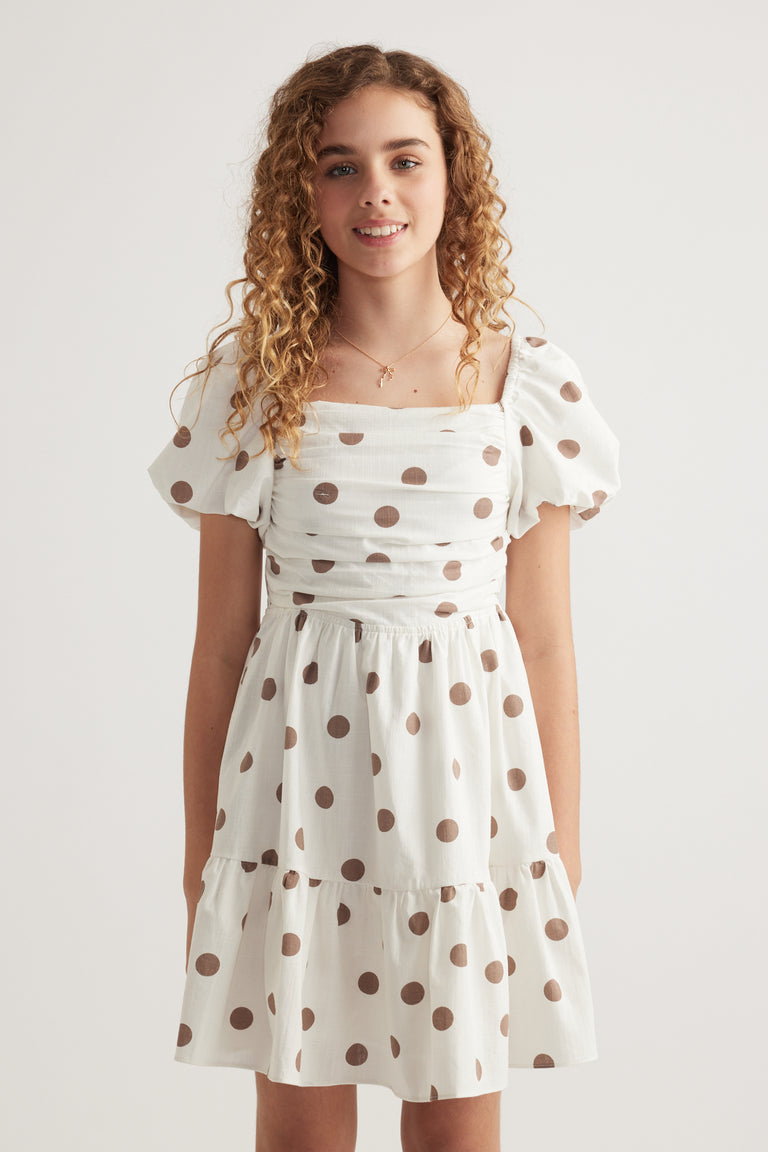 Girl wearing a white spot print dress with puff sleeves, square neckline and tiered skirt