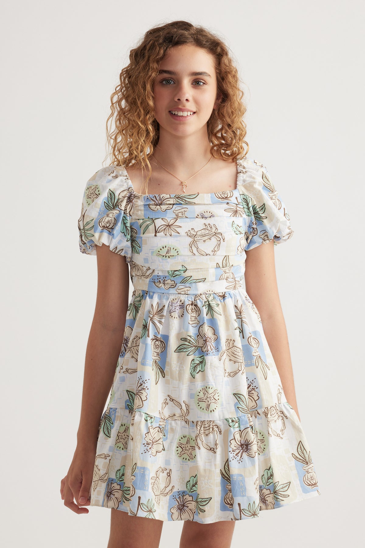 Girl wearing a floral print dress with puff sleeves, square neckline and tiered skirt