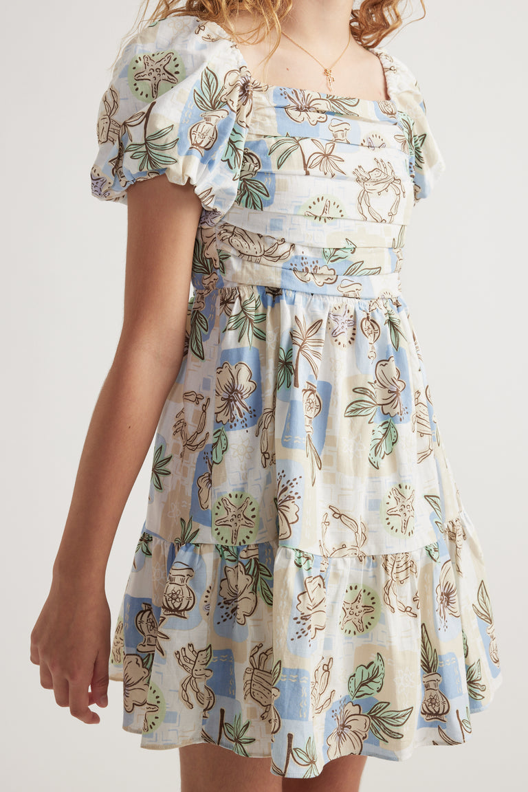 Girl wearing a light blue and cream spot print dress with puff sleeves, square neckline and tiered skirt