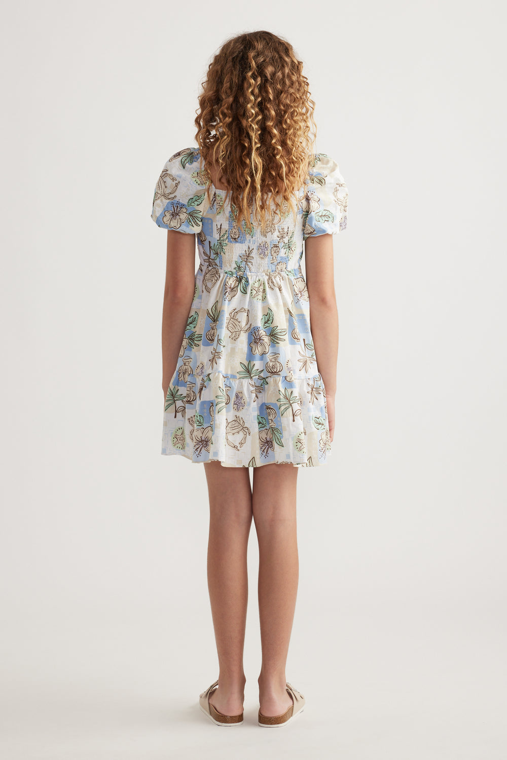Girl viewed from behind wearing a floral print dress with puff sleeves and a tiered skirt