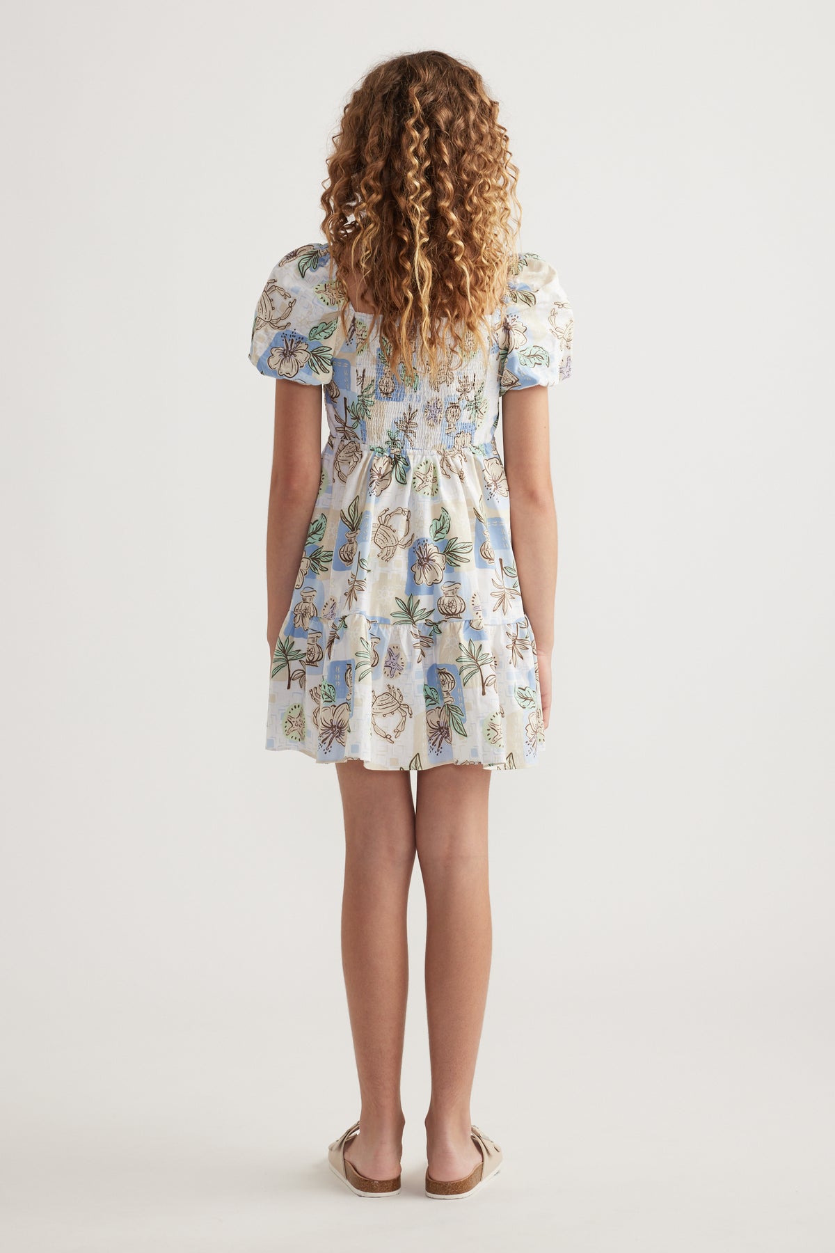 Girl viewed from behind wearing a floral print dress with puff sleeves and a tiered skirt