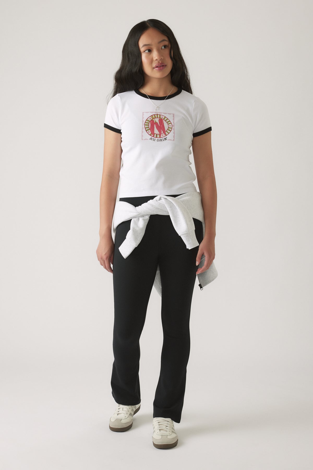 Girl in a white ringer tee with black trim and graphic front, styled with black fitted pants and tied sweatshirt at waist