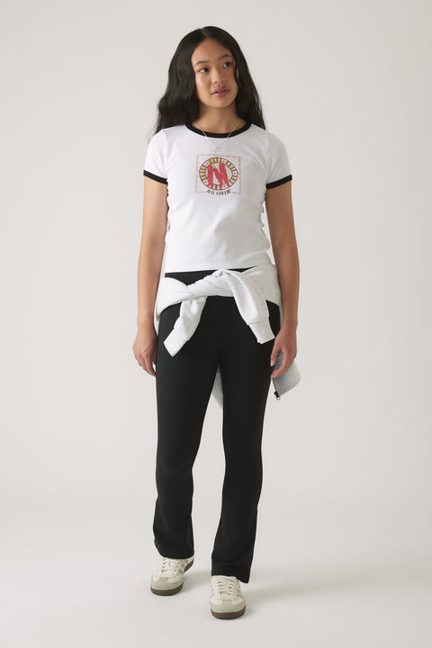 Girl in a white ringer tee with black trim and graphic front, styled with black fitted pants and tied sweatshirt at waist