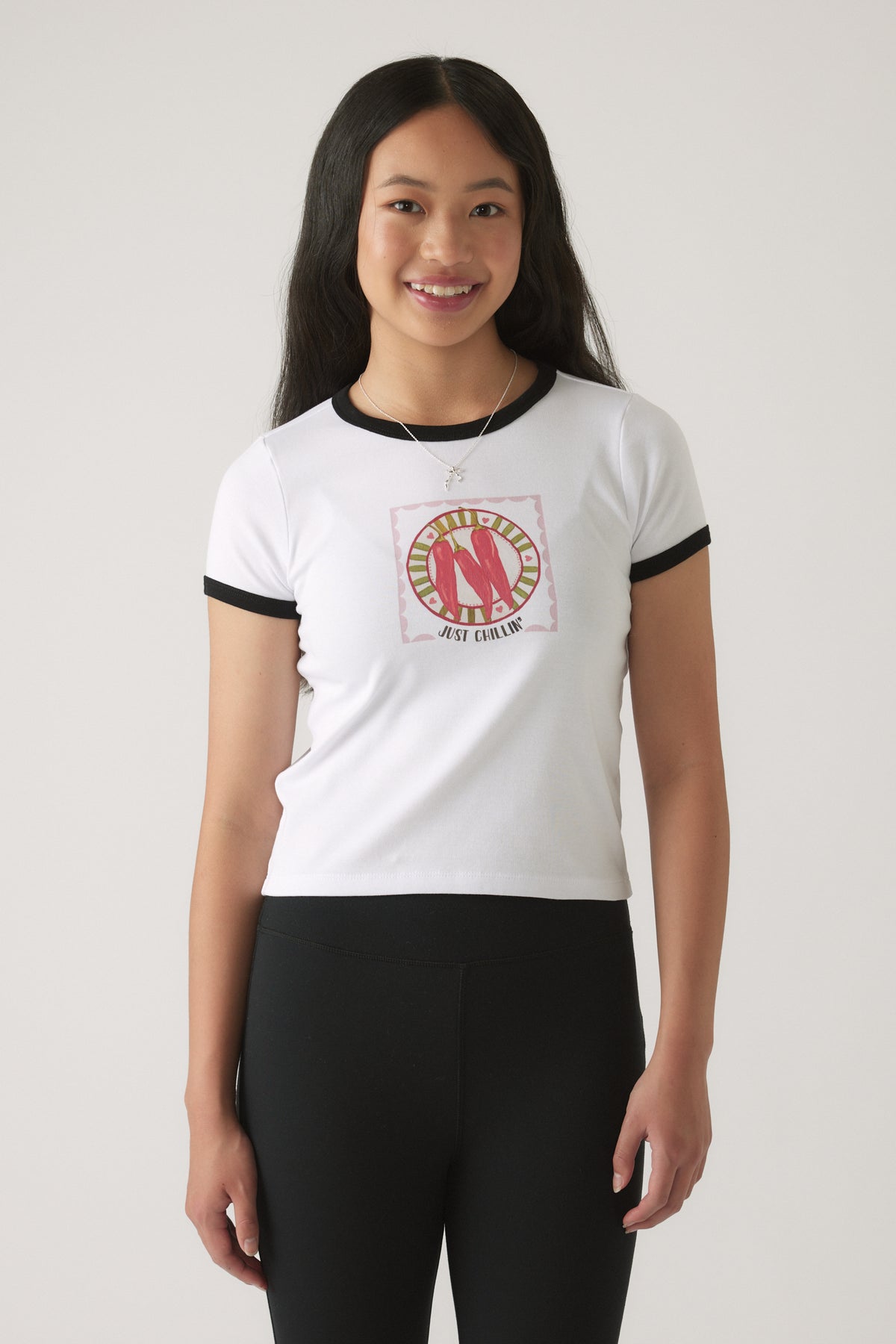 Girl wearing a white ringer tee with black trim and a red chillies graphic paired with black fitted pants