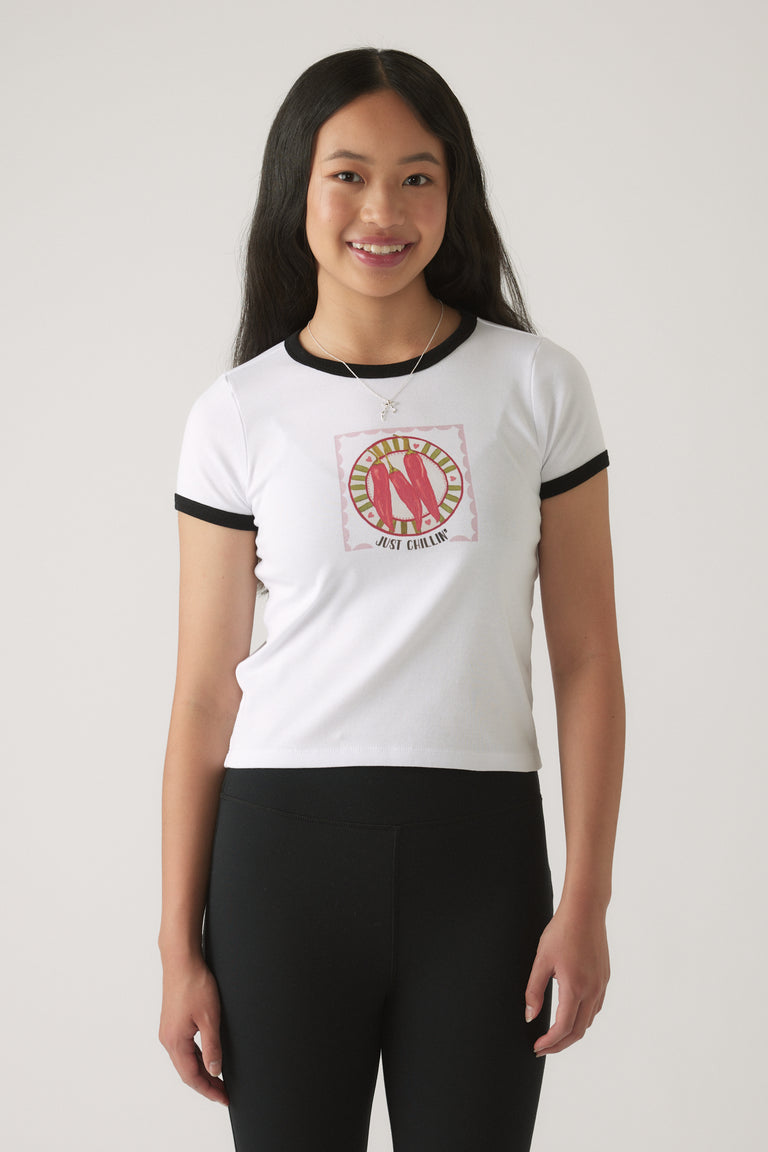 Girl wearing a white ringer tee with black trim and a red chillies graphic paired with black fitted pants