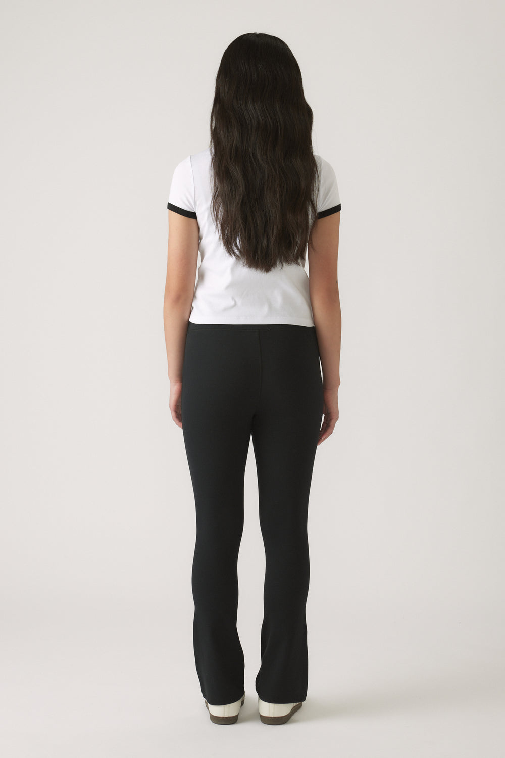 Back view of girl wearing a white tee with black trimming paired with fitted black pants and white sneakers