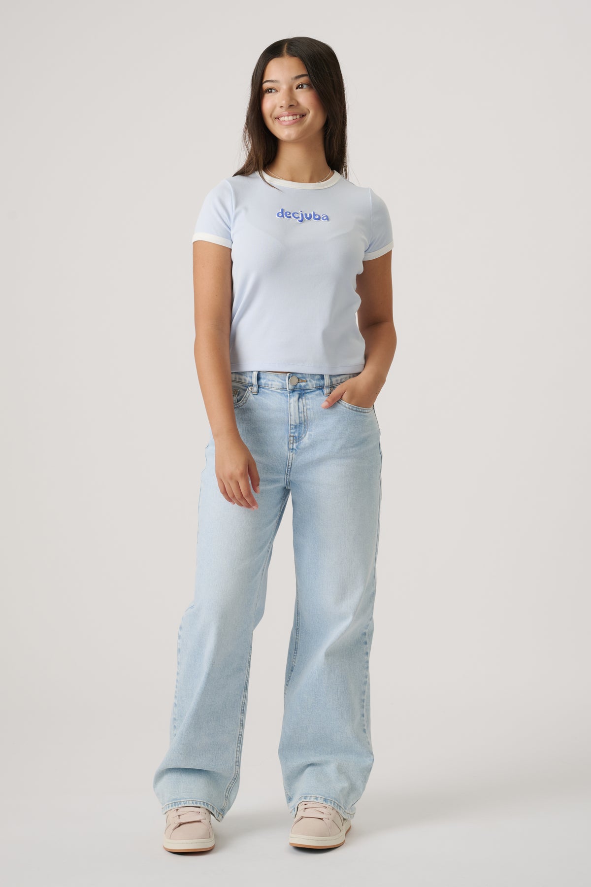 Teen girl wearing a sky blue cropped tee with logo paired with relaxed light wash wide-leg jeans and sneakers