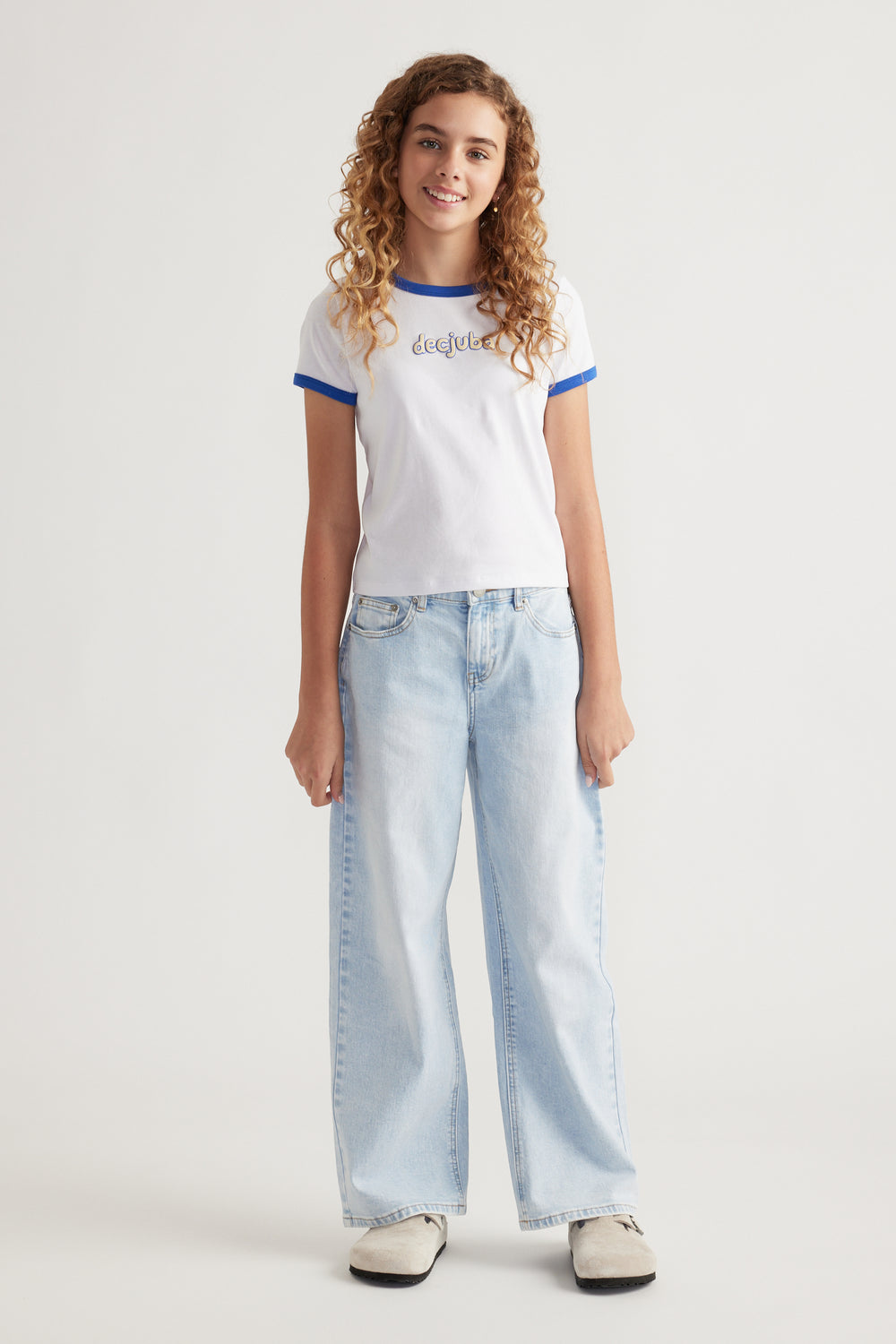 Young girl wearing a white cropped tee with blue trim and light wash wide-leg jeans and casual shoes