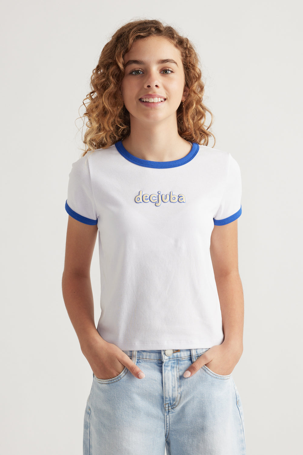 Girl wearing a white cropped tee with blue contrast trim and puff print logo paired with light wash denim jeans