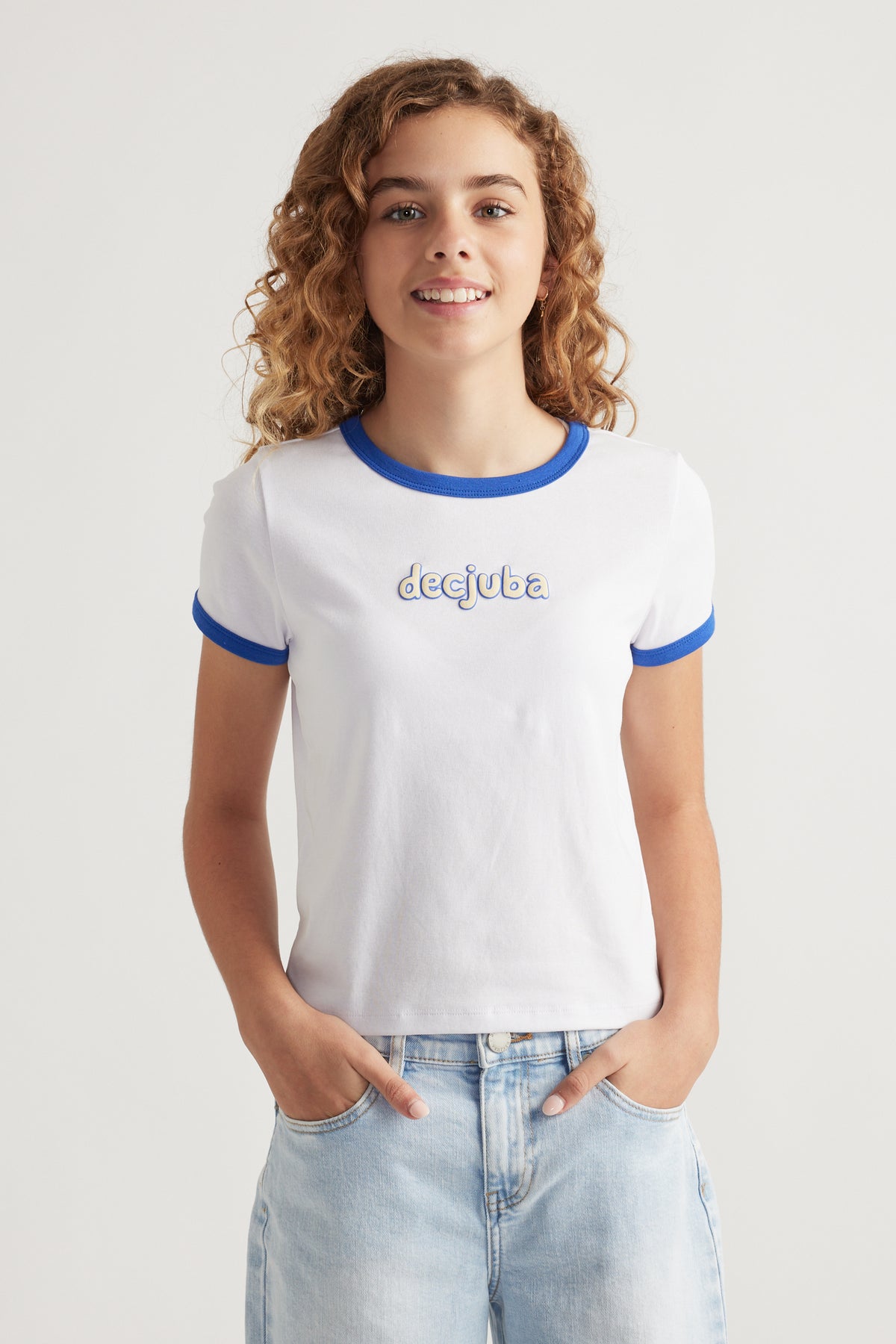 Girl wearing a white cropped tee with blue contrast trim and puff print logo paired with light wash denim jeans