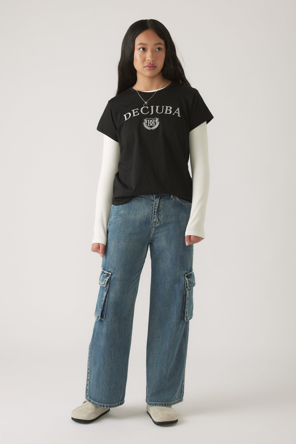 Teen girl wearing relaxed straight-leg blue denim cargo pants paired with layered black and white tops and white boots