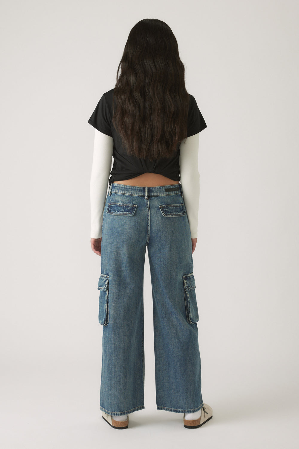 Girl shown from behind wearing relaxed blue denim cargo pants with side pockets and casual sneakers