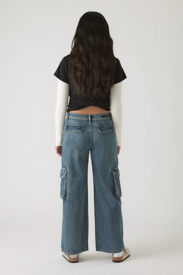 Girl shown from behind wearing relaxed blue denim cargo pants with side pockets and casual sneakers