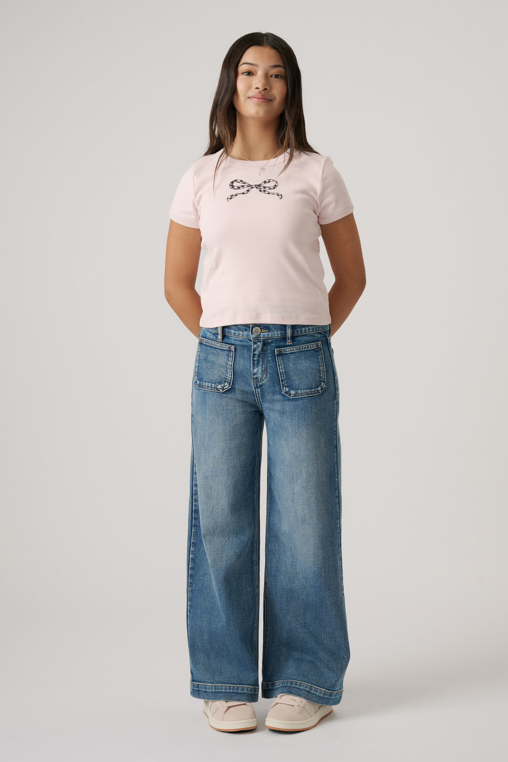 Girl wearing light wash wide-leg jeans with front patch pockets paired with a soft pink tee featuring a check bow graphic.