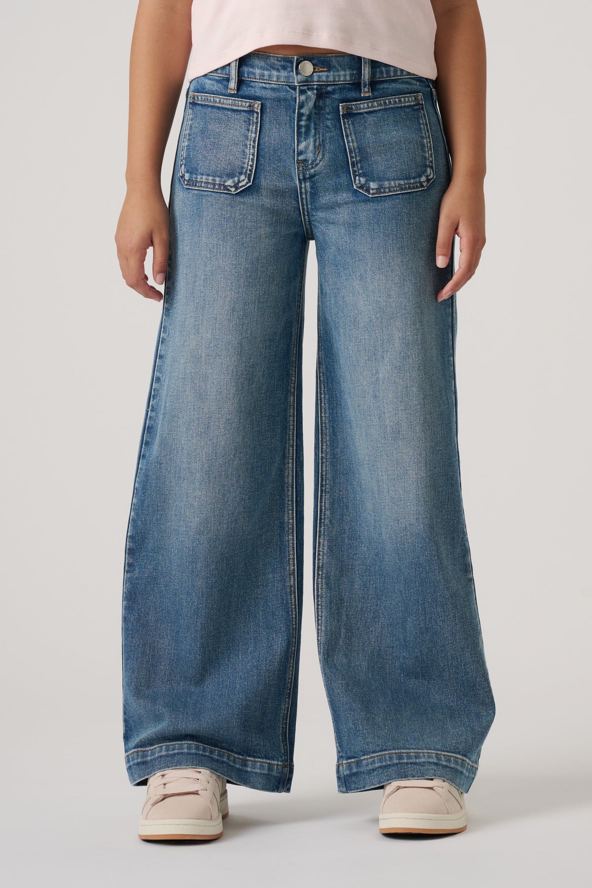 Girls wearing relaxed wide-leg blue denim jeans with front patch pockets and casual light sneakers.