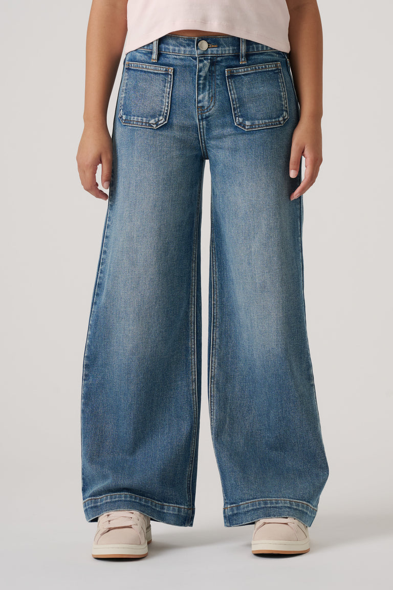 Girls wearing relaxed wide-leg blue denim jeans with front patch pockets and casual light sneakers.