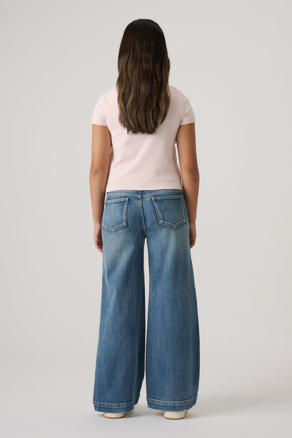 Girl seen from behind wearing light blue wide-leg denim jeans and a fitted pale pink short-sleeve top