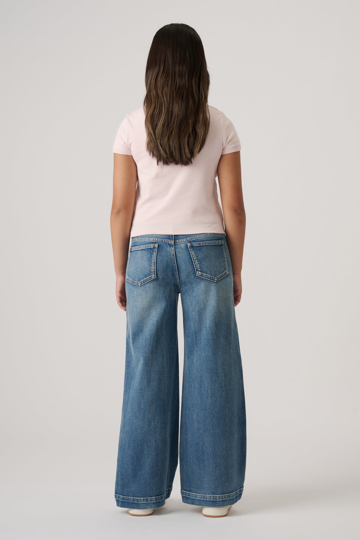 Girl seen from behind wearing light blue wide-leg denim jeans and a fitted pale pink short-sleeve top