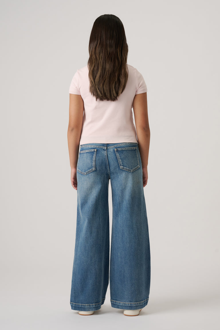 Girl seen from behind wearing light blue wide-leg denim jeans and a fitted pale pink short-sleeve top