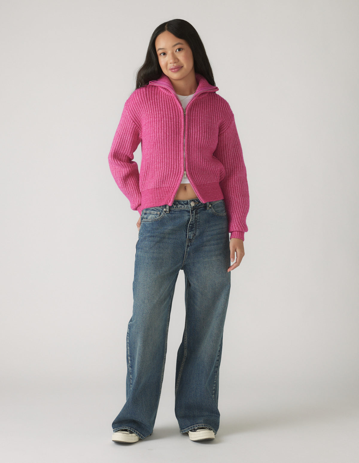 Girl wearing a bright pink zip-up knit jumper paired with relaxed wide-leg blue jeans and casual sneakers