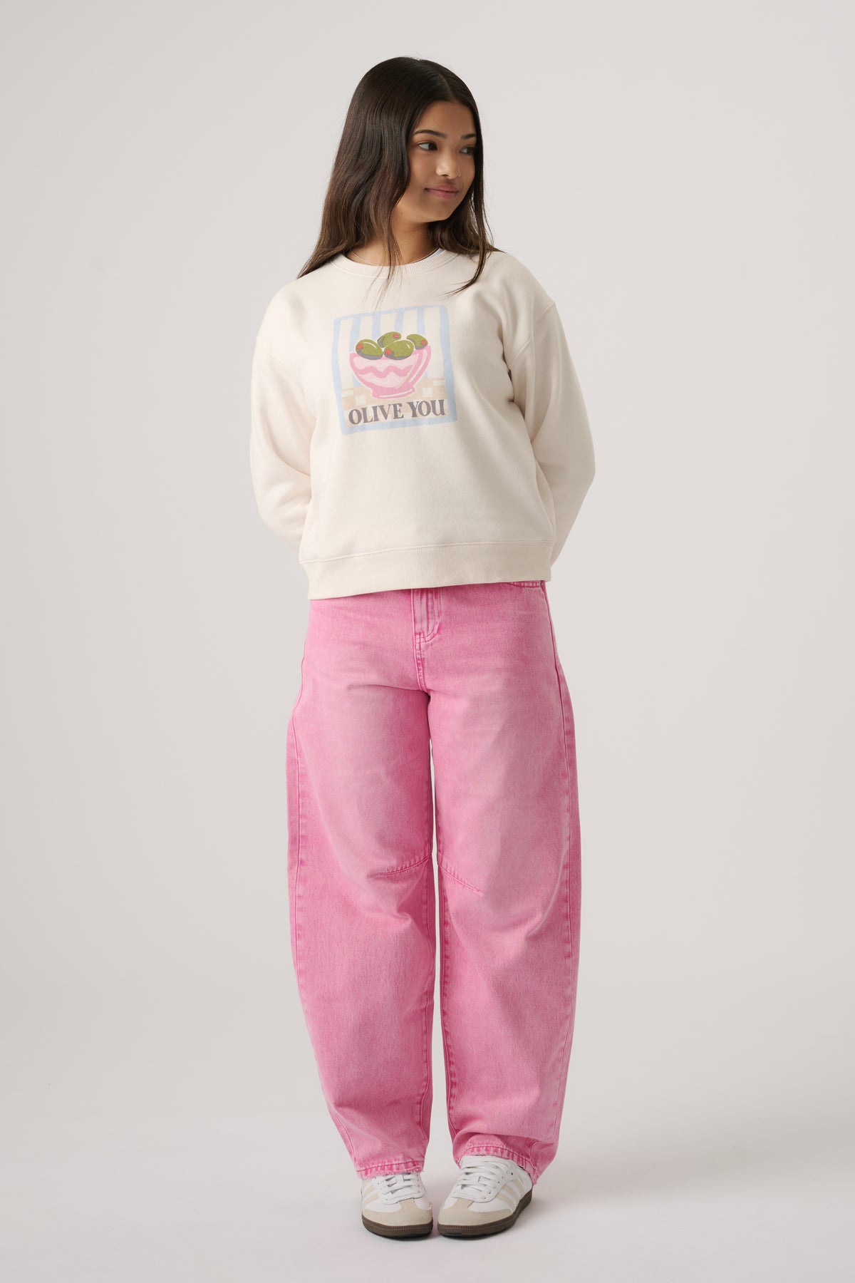 Girl wearing an off-white sweatshirt with olive graphic and wide-leg pink jeans paired with white sneakers