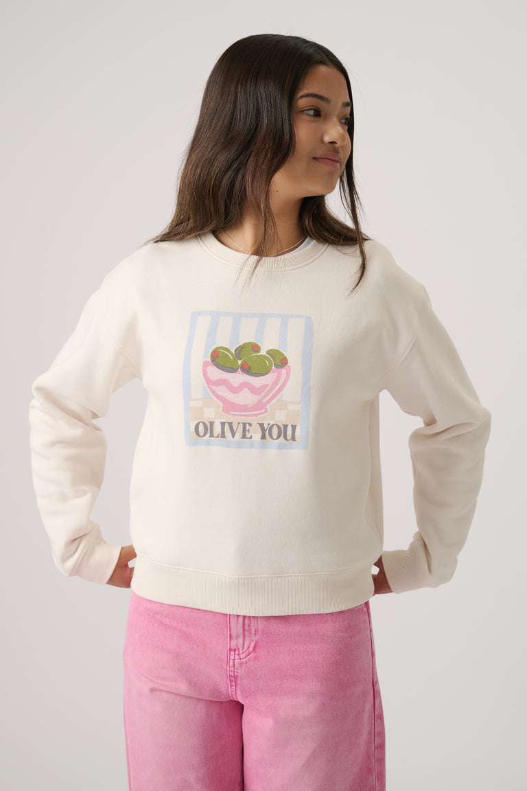 Girl wearing an off-white cropped sweatshirt with a playful olive bowl graphic and light pink jeans in a casual pose