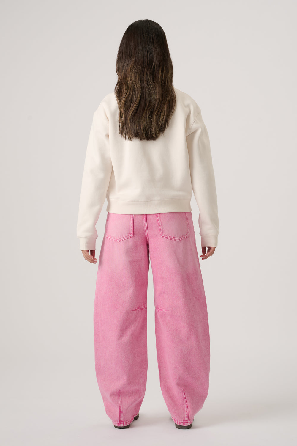 Girl wearing wide-leg pink denim jeans paired with an off-white cropped sweatshirt, viewed from behind
