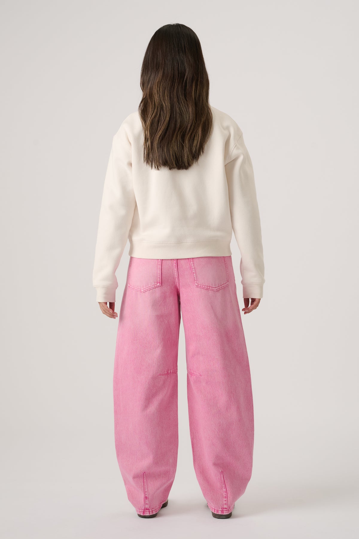 Girl wearing wide-leg pink denim jeans paired with an off-white cropped sweatshirt, viewed from behind