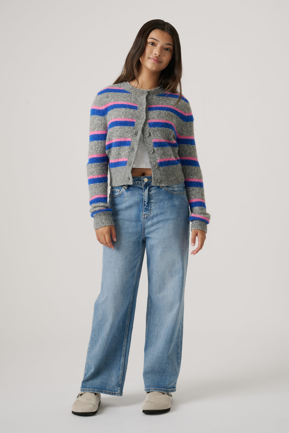 Teen girl wearing a cozy cropped cardigan with pink and blue stripes paired with loose light-wash denim jeans and beige shoes