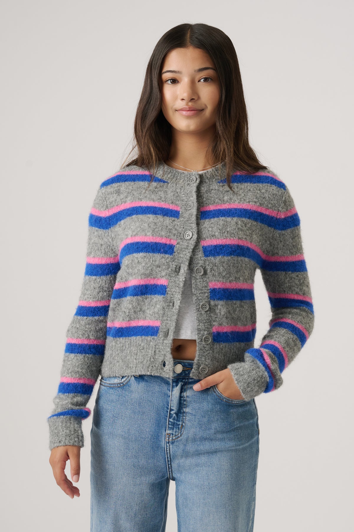 Teen girl wearing a cozy cropped cardigan with blue and pink stripes paired with casual light-wash denim jeans.
