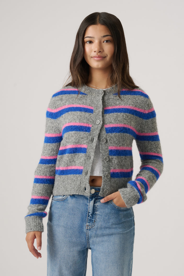 Teen girl wearing a cozy cropped cardigan with blue and pink stripes paired with casual light-wash denim jeans.