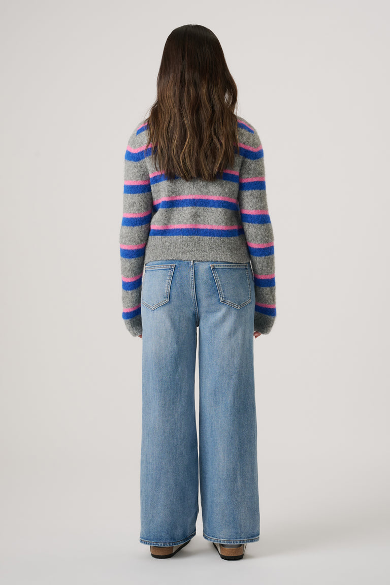 Girl seen from behind wearing a grey cardigan with blue and pink stripes and wide-leg light denim jeans