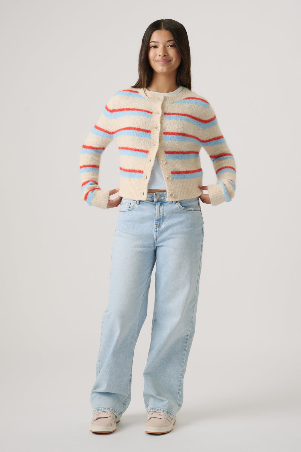 Girl wearing a cozy cropped cardigan with cream, red, and blue stripes paired with light wash wide-leg jeans and sneakers
