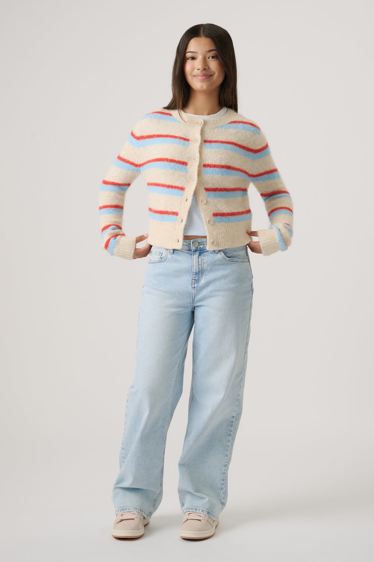 Girl wearing a cozy cropped cardigan with cream, red, and blue stripes paired with light wash wide-leg jeans and sneakers
