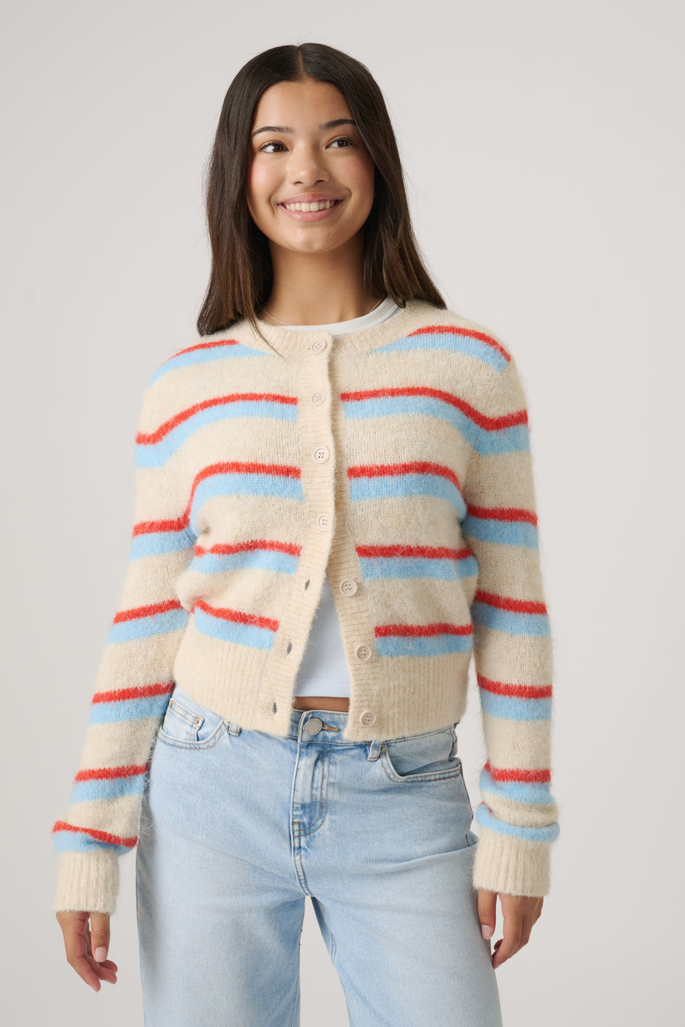 Young woman wearing a cozy cropped cardigan with colorful stripes paired with light wash high-rise jeans, smiling confidently.