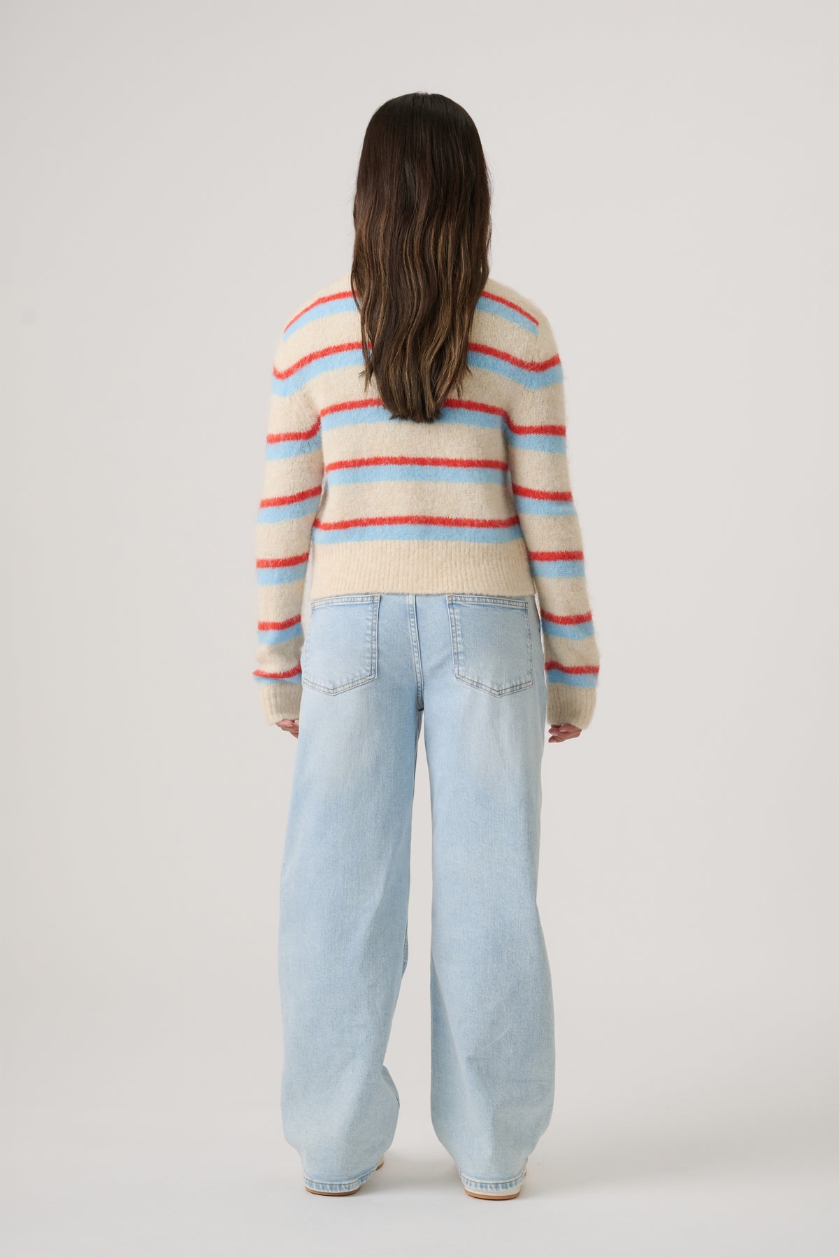 Girl wearing a soft striped cropped sweater paired with light wash wide-leg denim jeans, shown from behind.