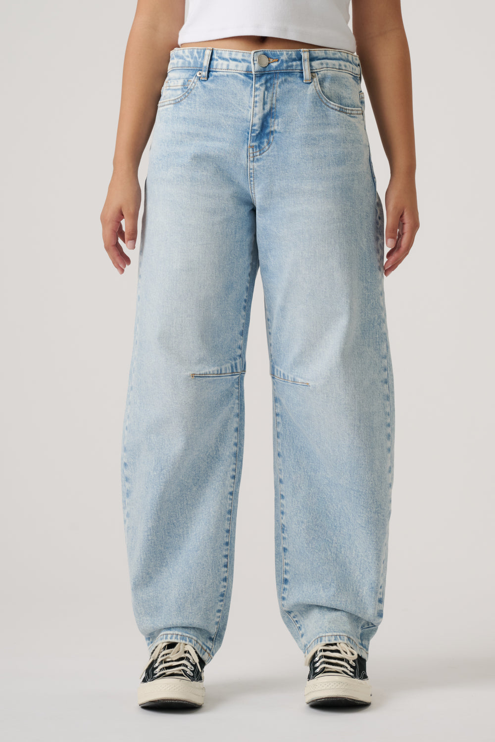 Light wash loose-fitting girls jeans with barrel leg cut paired with casual black and white sneakers.
