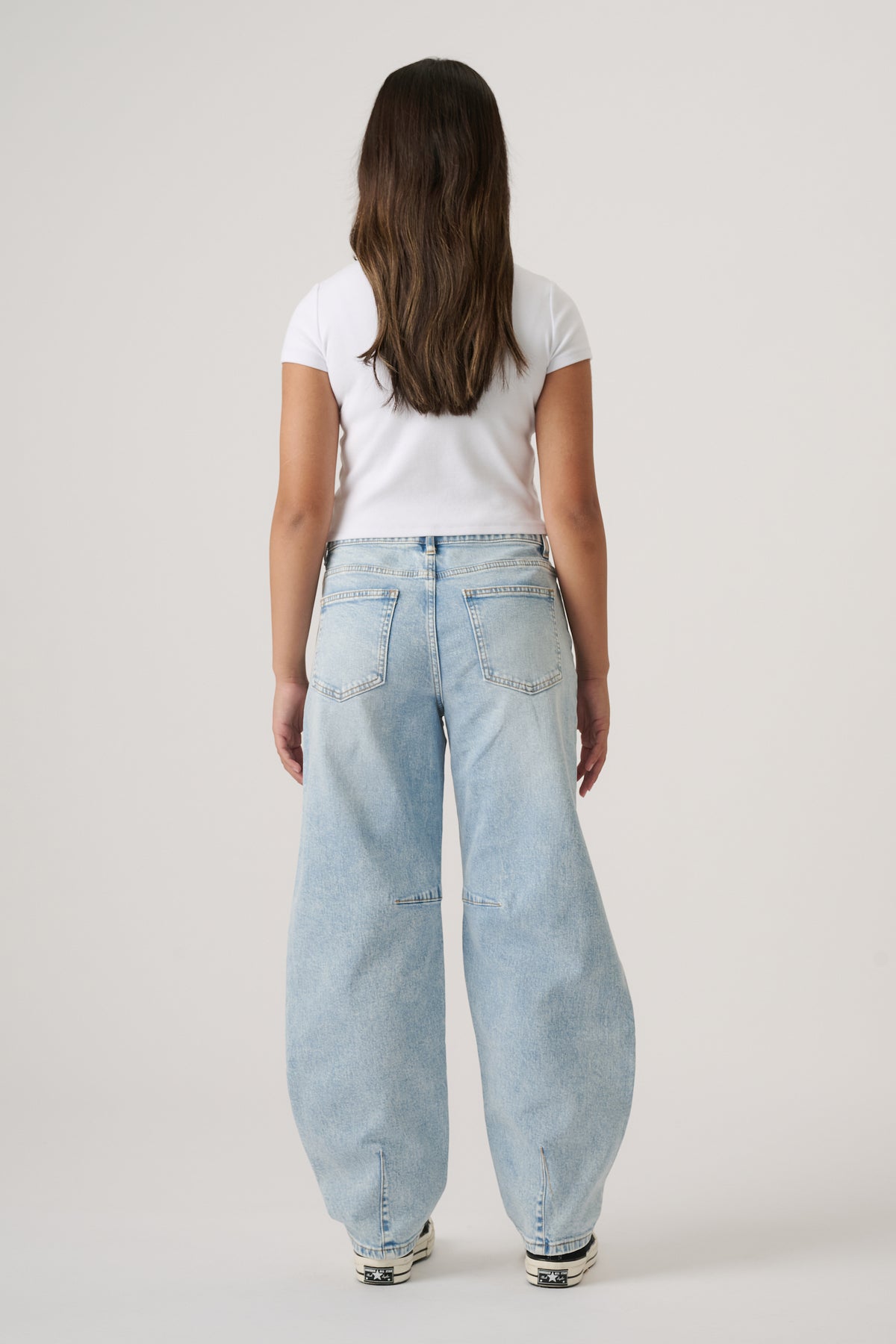 Girl wearing light blue wide-leg denim jeans paired with a fitted white short-sleeve top and sneakers viewed from behind