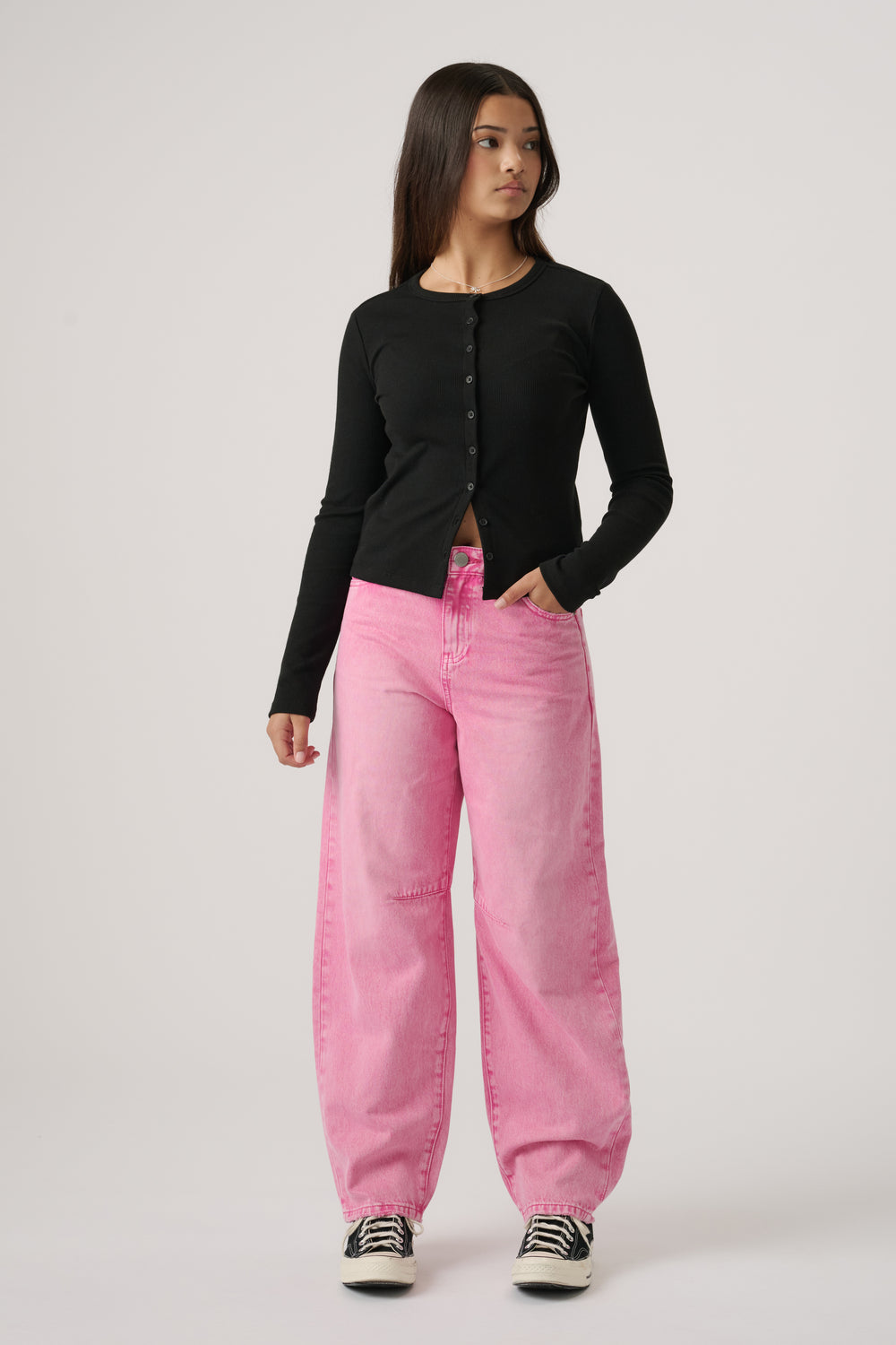 Teen girl wearing pink wide-leg jeans paired with a fitted black button-up top and sneakers