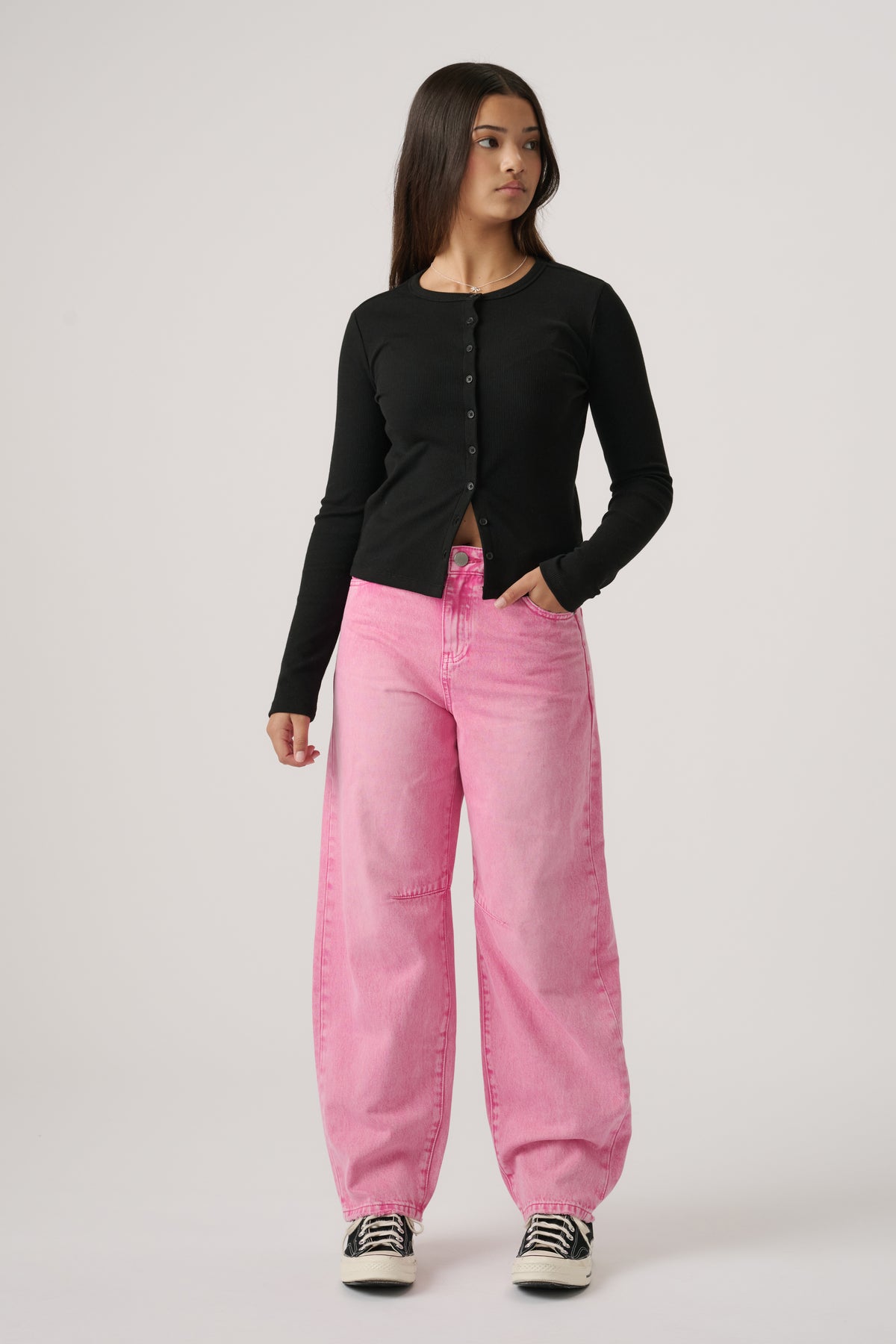 Teen girl wearing pink wide-leg jeans paired with a fitted black button-up top and sneakers