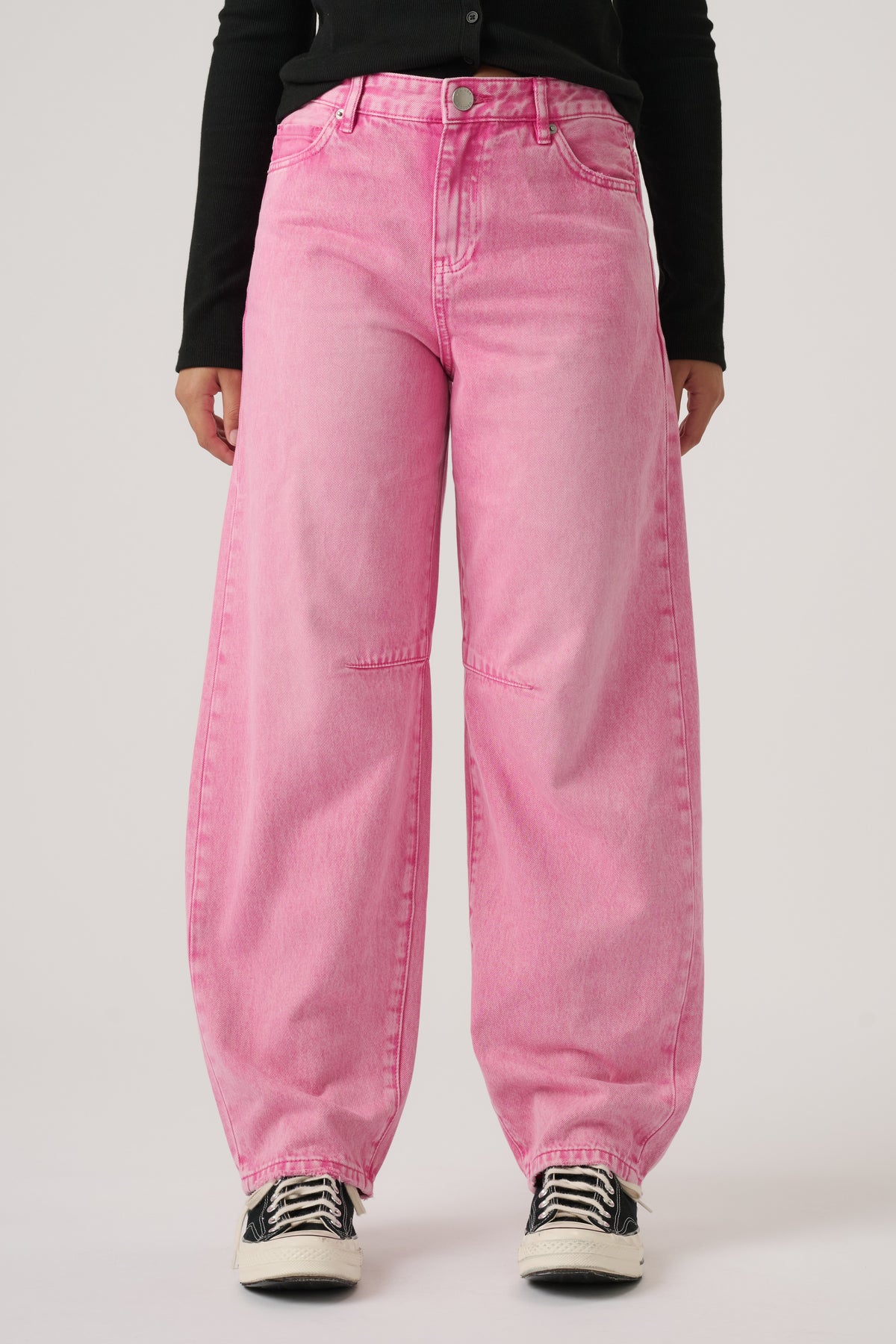 Girl wearing relaxed fit pink denim jeans paired with black long-sleeve top and black and white sneakers