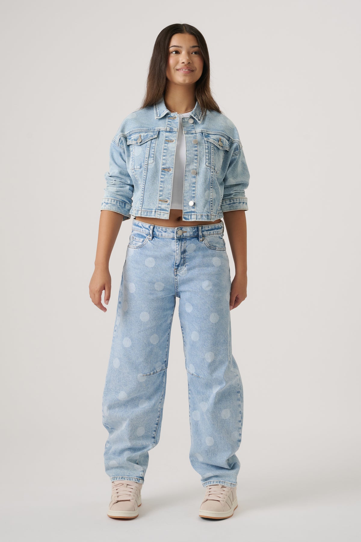 Teen girl wearing light wash denim jacket with rolled sleeves and relaxed polka dot wide-leg jeans and sneakers
