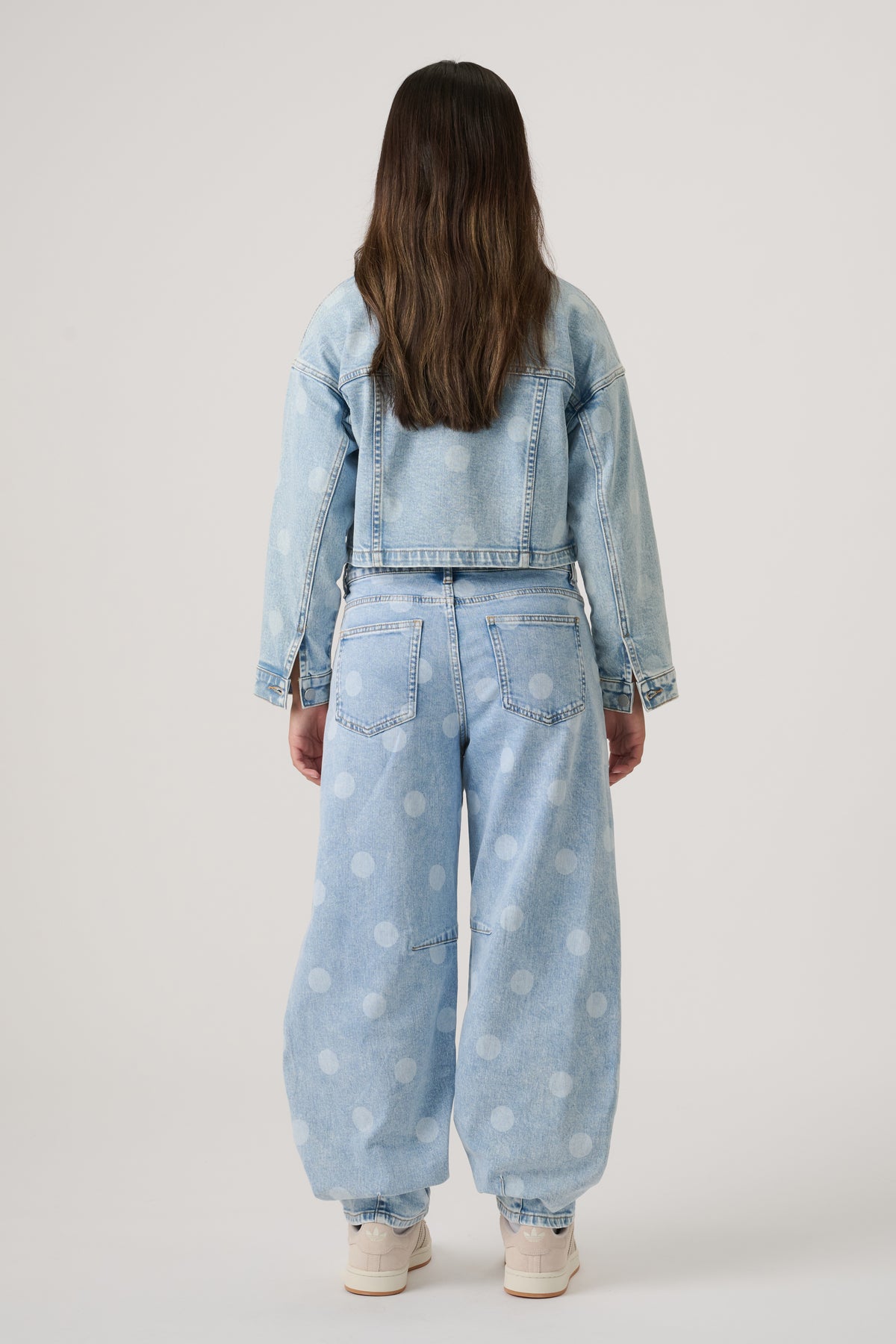 Girl wearing light blue denim barrel leg jeans with faded polka dots and matching cropped denim jacket