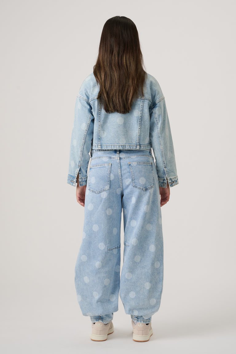 Girl wearing light blue denim barrel leg jeans with faded polka dots and matching cropped denim jacket