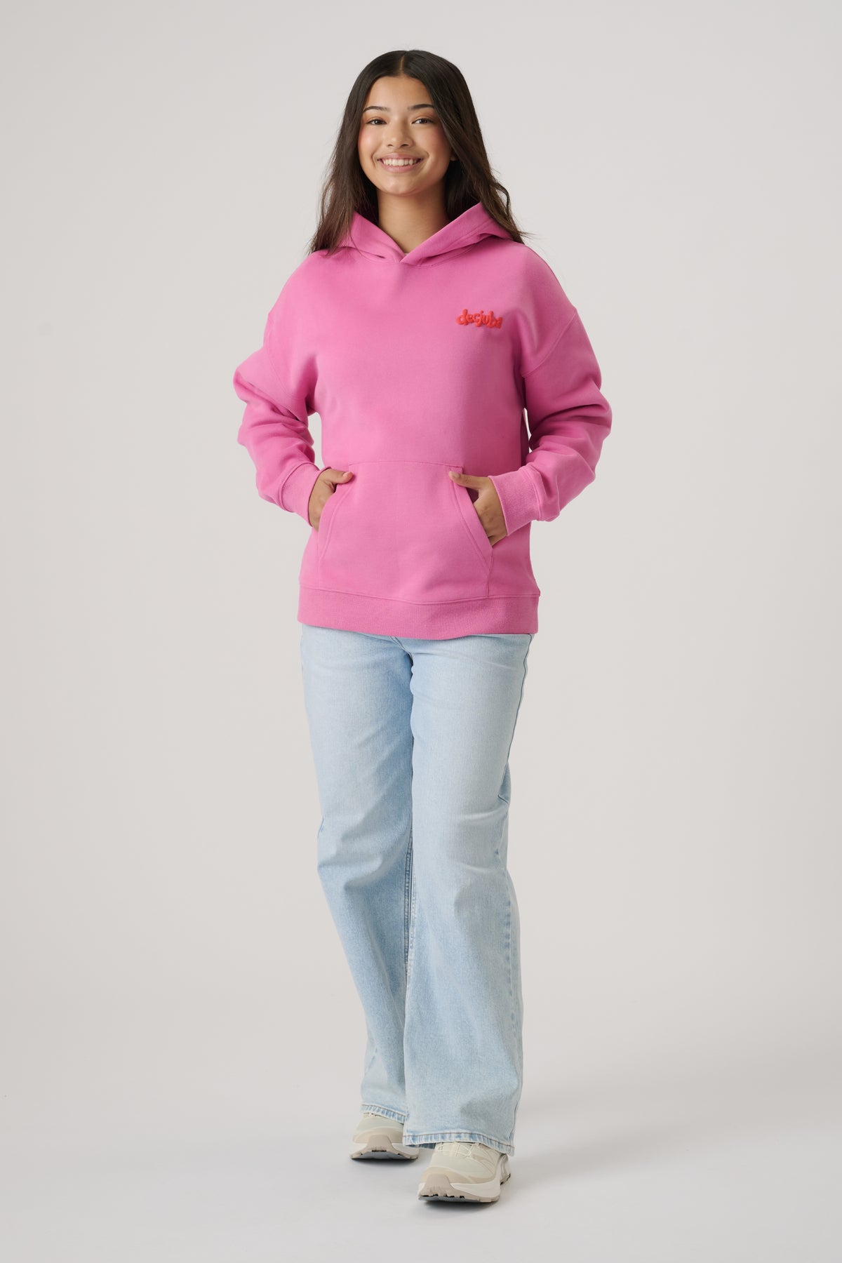 Teen girl smiling wearing a bright pink oversized hoodie paired with light washed wide-leg jeans and trainers