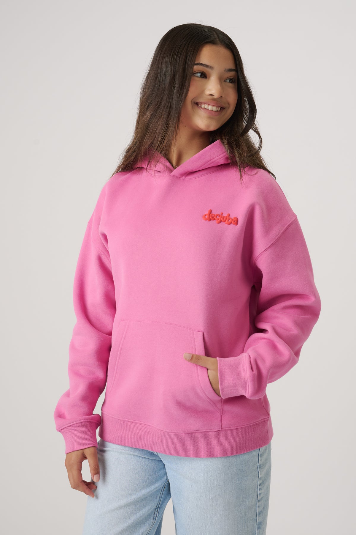 Teen girl wearing a bright pink oversized hoodie with kangaroo pocket, smiling with loose hair and light wash jeans