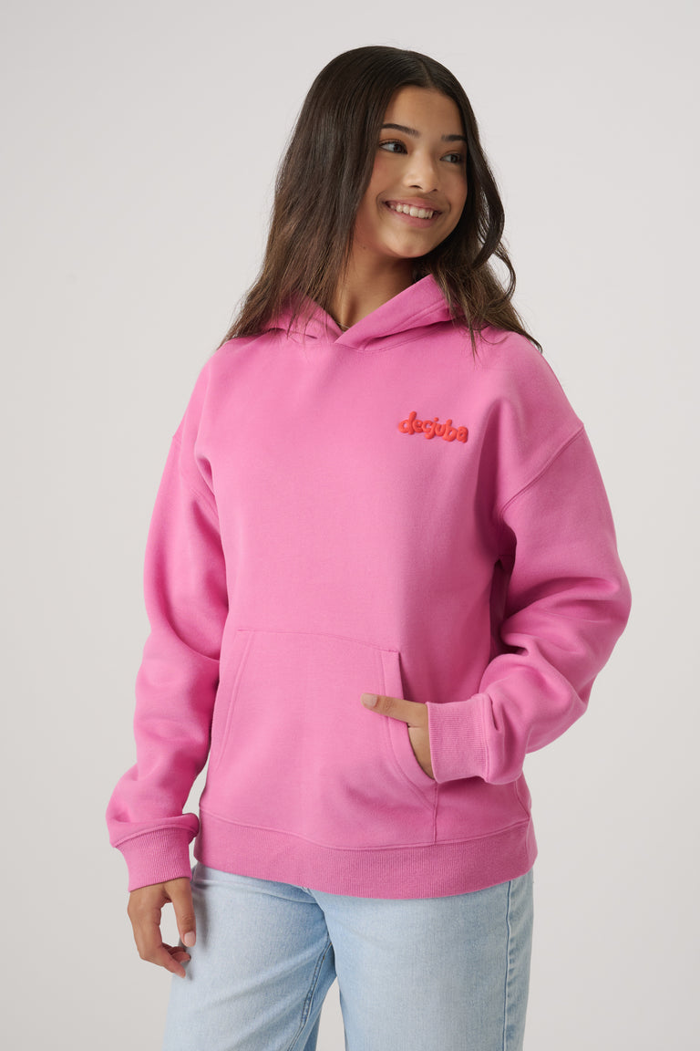 Teen girl wearing a bright pink oversized hoodie with kangaroo pocket, smiling with loose hair and light wash jeans