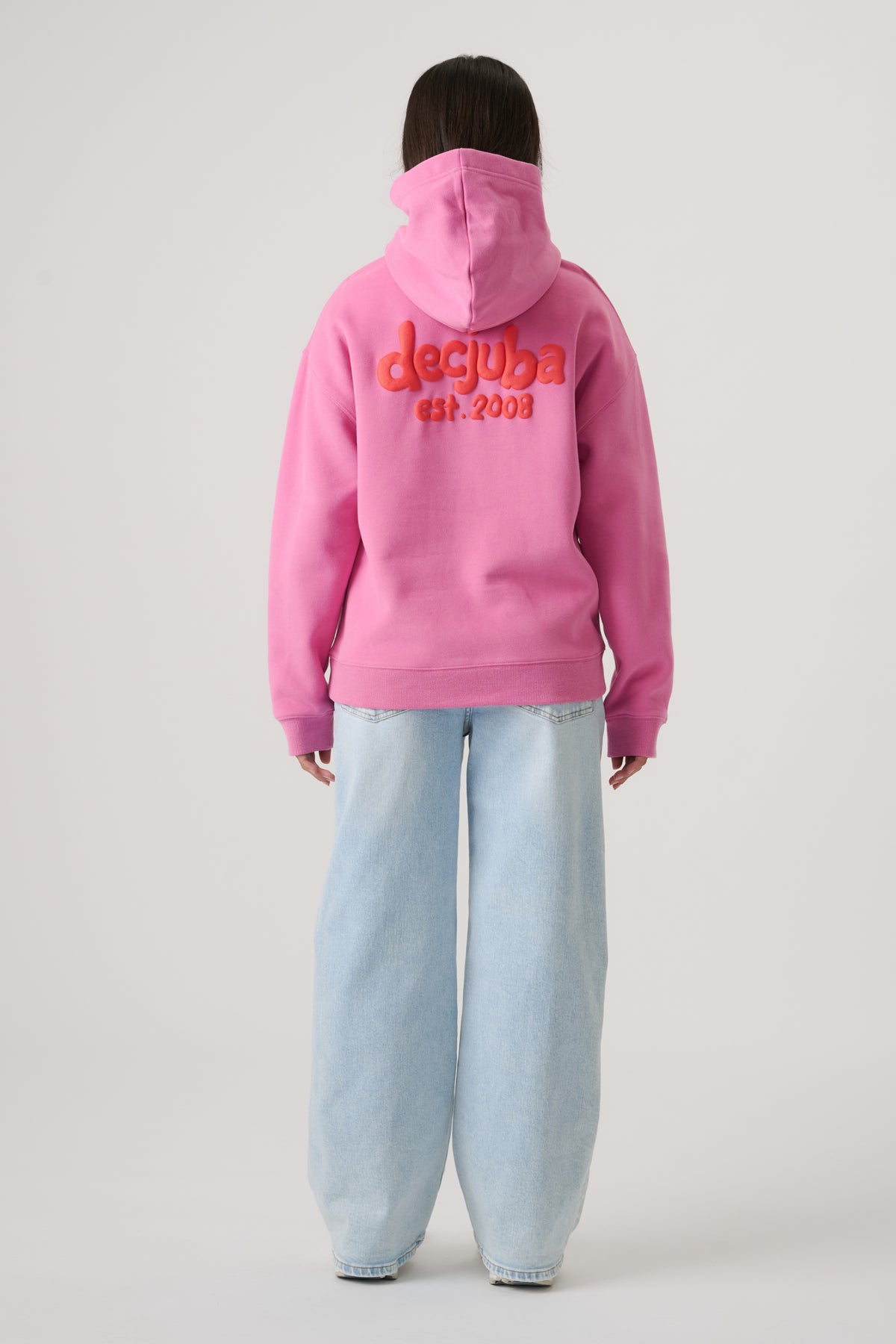 Girl wearing a bright pink oversized hoodie with logo detail paired with loose light-wash wide-leg jeans viewed from behind
